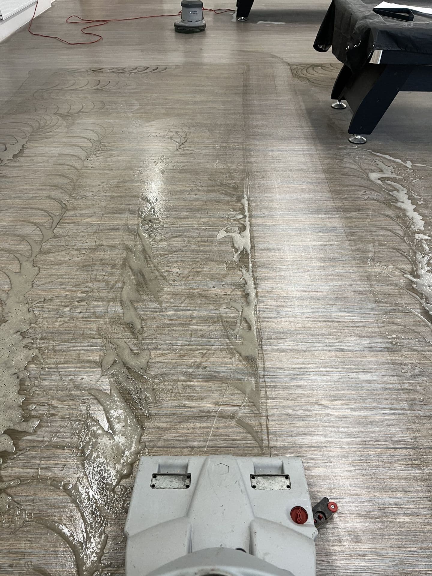 Floor scrubbing machine deep cleaning a hard floor in a communal games room
