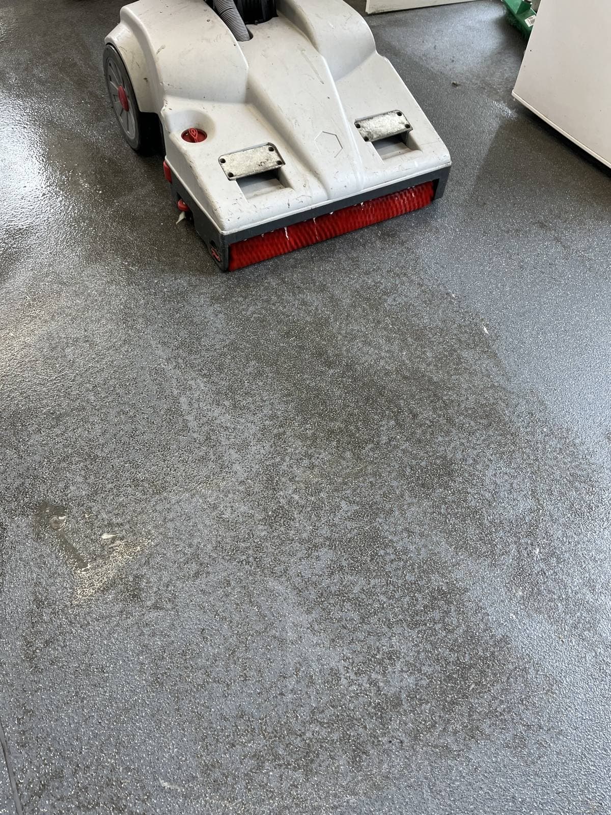 Scrubber dryer machine cleaning a grey resin floor