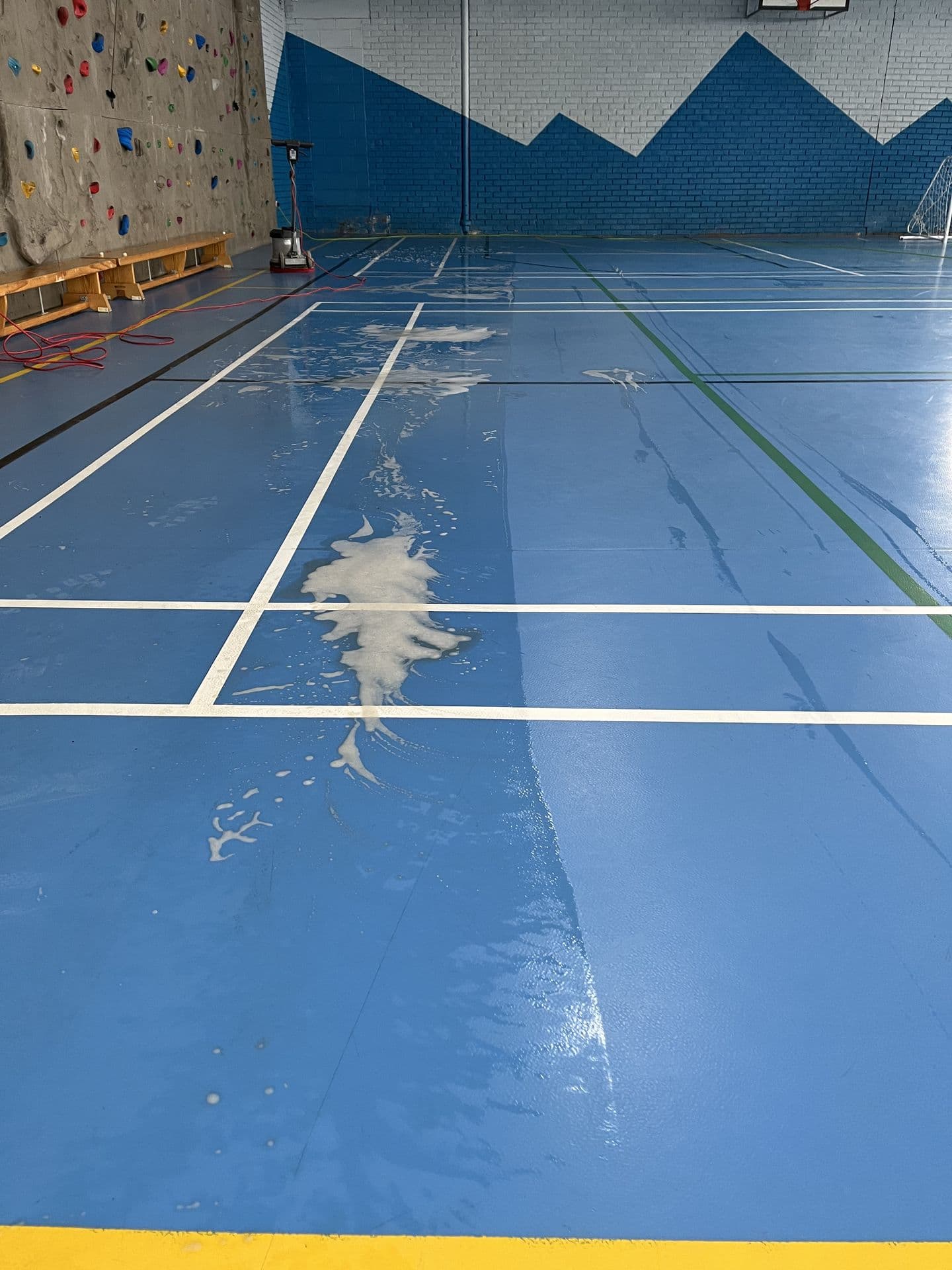 Sports hall floor being machine scrubbed, with a clean, glossy finish where the machine has passed